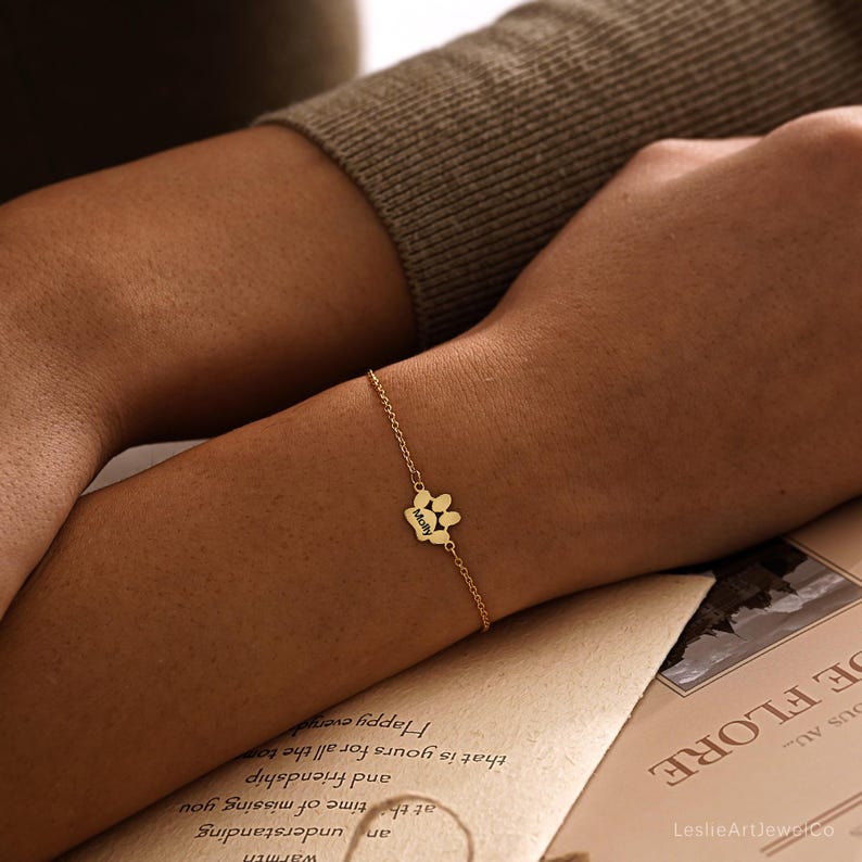 Pode incluir: Uma pulseira de corrente em tom dourado com um pingente central em forma de pata. O pingente est&aacute; gravado com o nome Molly em letra cursiva. A delicada corrente de metal conecta-se ao pingente em ambos os lados, criando uma joia simples.