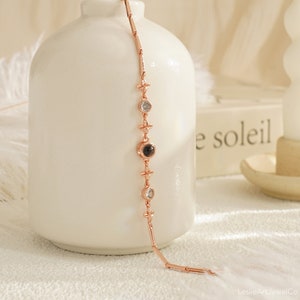 May include: A rose gold bracelet with a black stone and clear stones. The bracelet has a delicate chain with small cross-shaped charms.