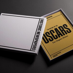 Puede incluir: Un libro cerrado con una cubierta blanca y texto negro que dice "Historic Newspapers: The History of the Oscars: Los Angeles Times". El libro est&aacute; abierto para revelar una cubierta amarilla con texto negro que dice "The History of the Oscars: Los Angeles Times".