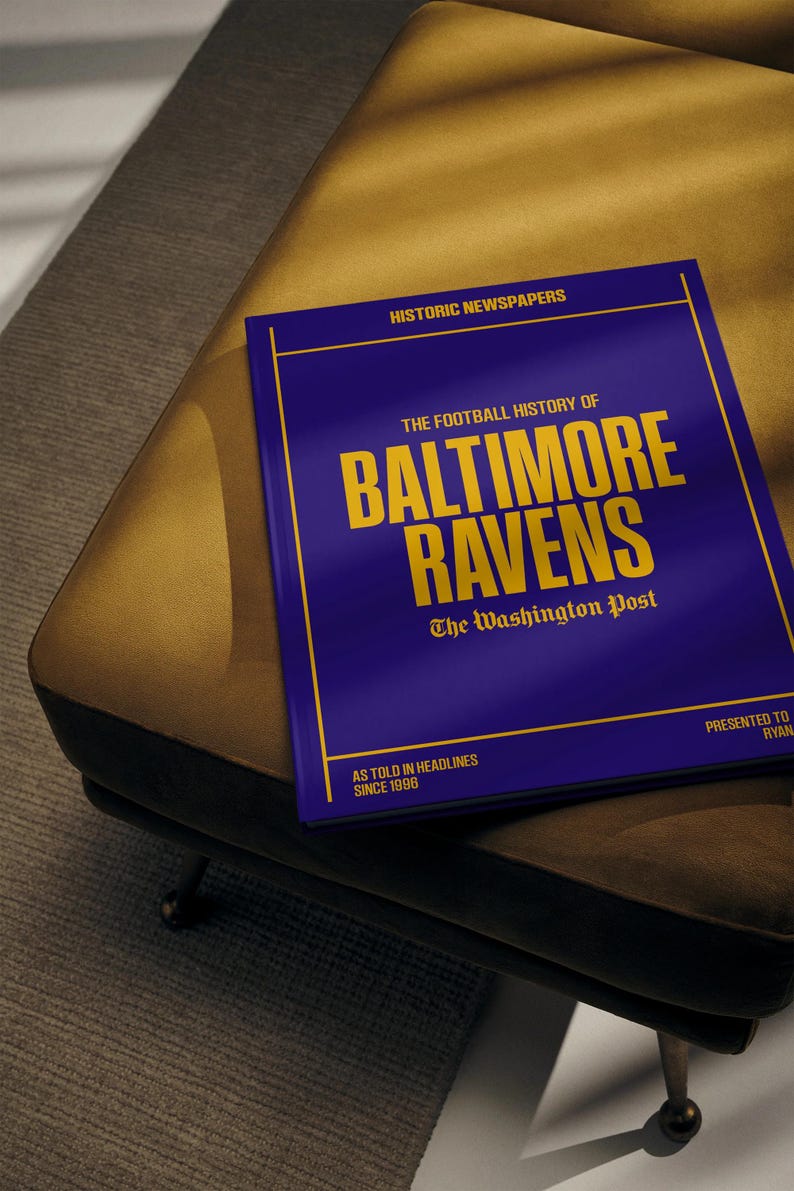 May include: A blue book with gold lettering titled "The Football History of Baltimore Ravens: The Washington Post, As Told in Headlines Since 1996".