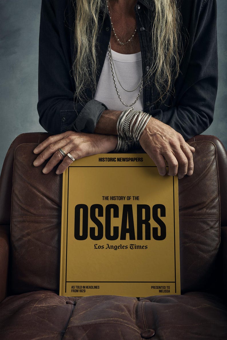 Puede incluir: Un libro amarillo con el t&iacute;tulo "The History of the Oscars" en letras negras. El libro es del Los Angeles Times y presenta titulares de 1920. El libro se presenta a Melissa.