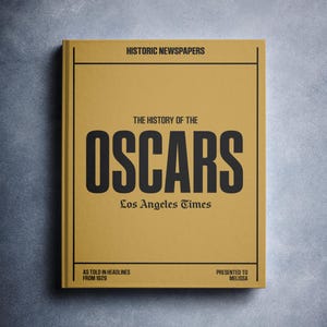 Puede incluir: Un libro amarillo titulado "The History of the Oscars" con el texto "Los Angeles Times" y "As Told in Headlines from 1929" impreso en la portada.