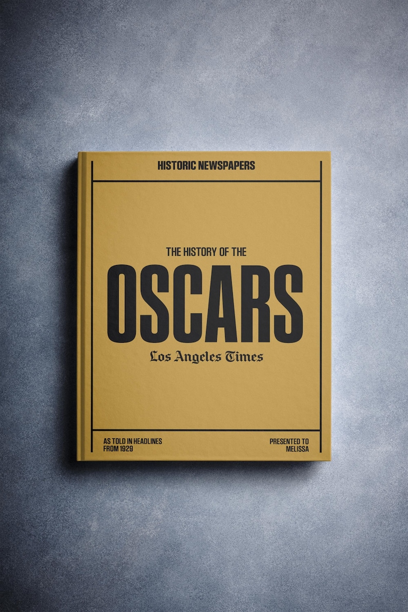 Puede incluir: Un libro amarillo titulado "The History of the Oscars" con el texto "Los Angeles Times" y "As Told in Headlines from 1929" impreso en la portada.