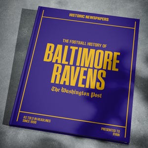 May include: A purple book with the title "The Football History of Baltimore Ravens" in yellow text. The book is presented to Ryan and features the Washington Post logo.
