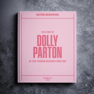 May include: A pink book with the title "The Story of Dolly Parton" and the subtitle "As Told Through Headlines Since 1967". The book is presented to Leslie.