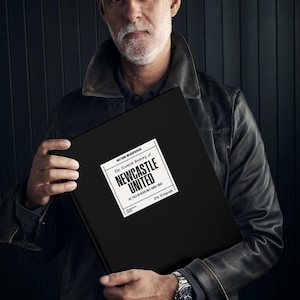 May include: A person holding a black book with the title "The Football History of Newcastle United As Told in Headlines Since 1892 The Telegraph" printed in white.