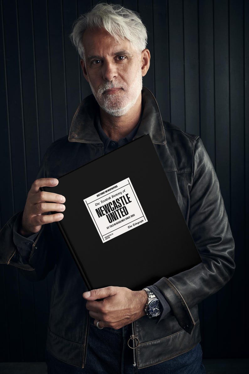 May include: A person holding a black book with the title "The Football History of Newcastle United As Told in Headlines Since 1892 The Telegraph" printed in white.