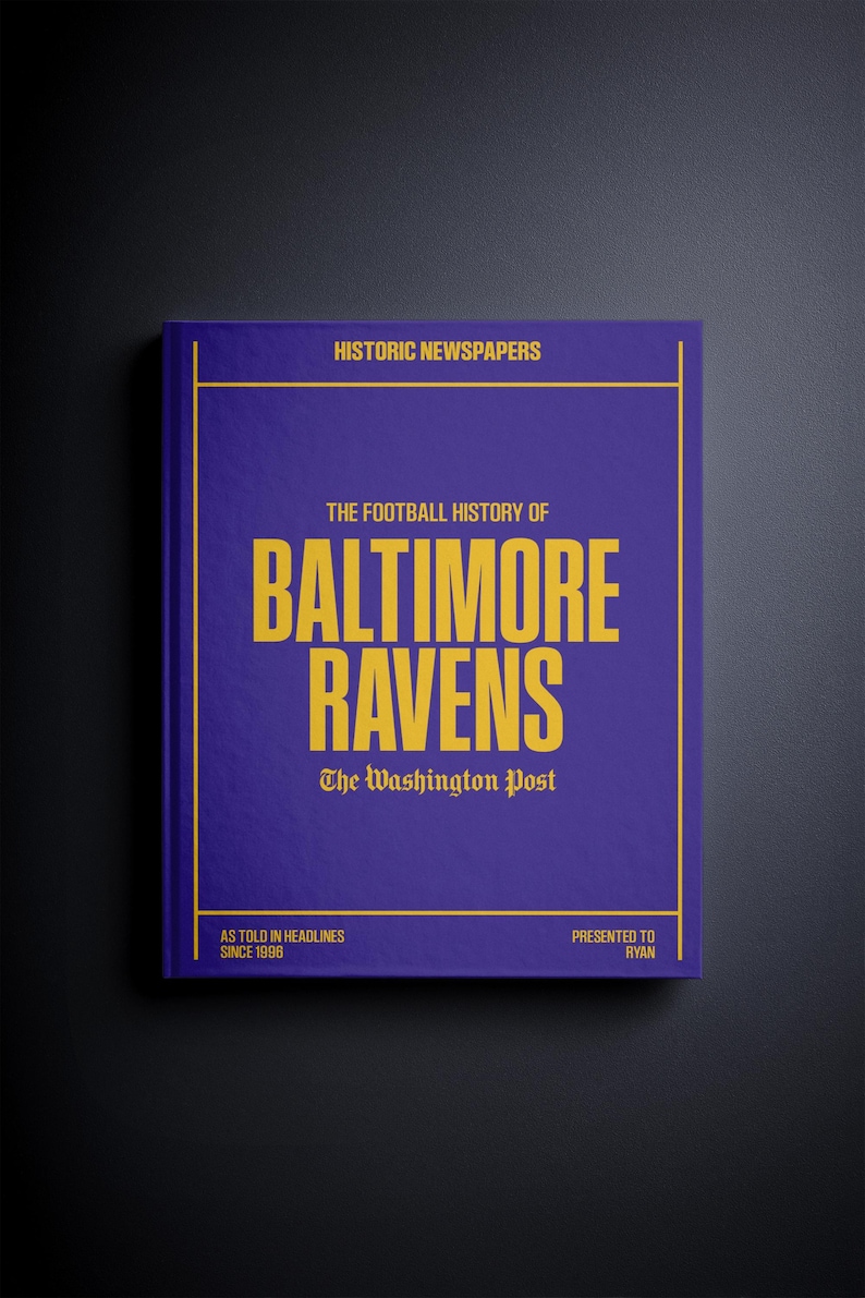 May include: A purple book with gold lettering titled "The Football History of Baltimore Ravens" by The Washington Post. The book is presented to Ryan and features headlines from 1998.