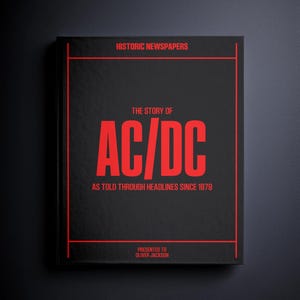 May include: A black book with red text and accents. The cover reads "HISTORIC NEWSPAPERS" at the top, with "THE STORY OF AC/DC" in large red letters. Below, it says "AS TOLD THROUGH HEADLINES SINCE 1979." The book is presented to Oliver Jackson.