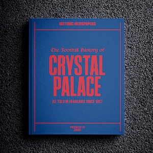 Op de afbeelding: Een blauw boek met de titel "The Football History of Crystal Palace" in rode tekst. De ondertitel is "As Told in Headlines Since 1907".