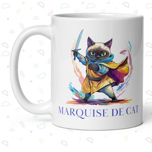 May include: White ceramic mug with a colorful illustration of a cat holding a sword. The cat is wearing a blue and yellow costume and has a purple cape. The text "MARQUISE DE CAT" is printed in blue below the image.