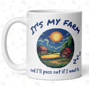 Könnte beinhalten: Weiße Keramiktasse mit einer blauen Grafik einer pixelartigen Farmlandschaft mit dem Text "IT'S MY FARM and I'll pass out if I want to" in blau.