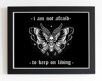May include: Black framed art print with a white moth design, incorporating a skull and the text "i am not afraid to keep on living". The moth illustration has intricate wing patterns, set against a black background.