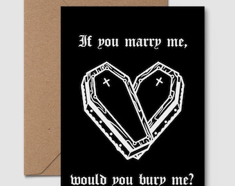 May include: A black greeting card with a brown envelope. The card features a white illustration of two coffins forming a heart shape, with the text "If you marry me, would you bury me?" in a gothic font.