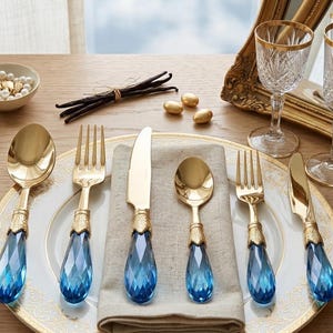 Juego de cubiertos de lujo de 36 piezas de acero inoxidable con cristal azul y detalles dorados, presentado en caja de regalo.