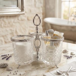 May include: A three-sectioned, silver-toned vanity organizer with clear glass containers. One section holds cotton pads, another has a perfume bottle and bath oil, and the third has cotton swabs. The organizer sits on a marble surface.