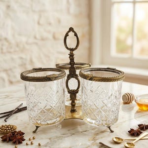 May include: A three-section serving dish with a brass-colored metal frame and handle. The clear glass containers have a diamond pattern. The dish sits on a marble surface, with spices and honey nearby.