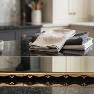 Puede incluir: Una bandeja rectangular con espejo que presenta un marco de metal dorado decorativo con asas de volutas ornamentadas y un borde festoneado. La bandeja tiene una superficie de vidrio reflectante y está colocada sobre granito oscuro.