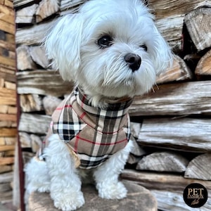 May include: A small white dog wearing a brown, black, and red plaid dog sweater. The dog is sitting on a wooden surface. The text "PET FASHION store" is visible in the lower right corner of the image.
