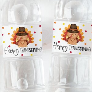 May include: Two clear plastic water bottles with labels that say "Happy Thanksgiving!" and feature a cartoon turkey wearing a pilgrim hat. The labels have a white background with red and yellow polka dots.