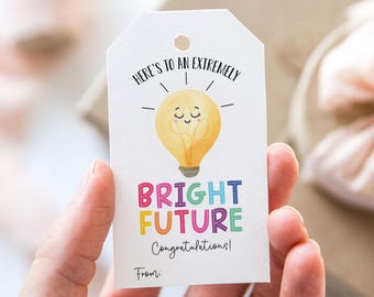 Op de afbeelding: Een wit cadeau-etiket met een afbeelding van een gloeilamp en de tekst "Here's to an extremely bright future! Congratulations! From:"
