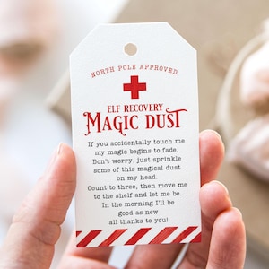 Puede incluir: Una etiqueta blanca con rayas rojas y blancas de bastón de caramelo en la parte inferior. La etiqueta dice "NORTH POLE APPROVED" y tiene un signo más rojo. El texto "ELF RECOVERY MAGIC DUST" está en rojo y blanco. La etiqueta tiene instrucciones para usar el polvo mágico para ayudar a un elfo a recuperarse.