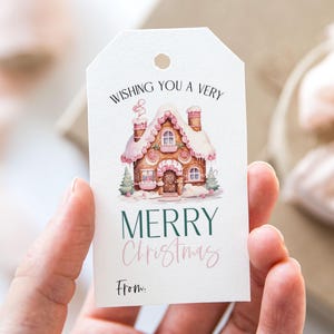May include: A white gift tag featuring a pink and white gingerbread house illustration. The text reads "Wishing you a very Merry Christmas" with a pink "Christmas" and "From:" at the bottom.