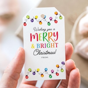 May include: White gift tag with colorful string lights and the text "Wishing you a MERRY & BRIGHT Christmas!" in various colors. The tag has a hole at the top for attaching to a gift. The bottom of the tag has the word "FROM:" printed on it.