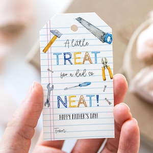 Könnte beinhalten: Ein Vatertags-Geschenkanhänger mit einer Aquarell-Illustration von Werkzeugen. Der Anhänger trägt die Aufschrift "A little TREAT for a dad so NEAT! HAPPY FATHER'S DAY!" in blauen und gelben Buchstaben. Der Anhänger wird in einer Hand gehalten.