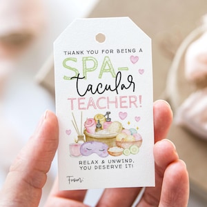 May include: A white gift tag with the text "THANK YOU FOR BEING A SPA-tacular TEACHER!" in green and pink. The tag features spa-themed illustrations, including a bowl of bath products, a sleep mask, and hearts. The text "RELAX & UNWIND. YOU DESERVE IT!" is also present.
