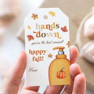 May include: A white rectangular gift tag with a hole at the top, featuring orange and brown autumn leaves, a yellow soap dispenser illustration with a small pumpkin, and the text: hands down you're the best around! happy fall! From: