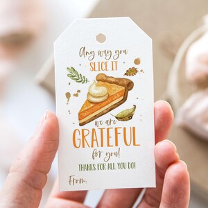 May include: A white gift tag with a watercolor illustration of a slice of pumpkin pie. The text reads "Any way you slice it, we are grateful for you! Thanks for all you do! From:"