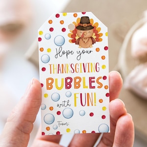 Può includere: Etichetta regalo bianca con un tacchino dei cartoni animati che indossa un cappello da pellegrino. L'etichetta ha un motivo a pois colorati e il testo "Spero che le tue bolle del Ringraziamento siano DIVERTENTI!" con spazio per "Da:"