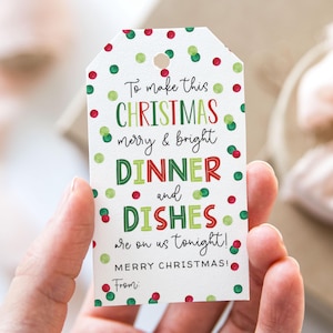 Puede incluir: Una etiqueta de regalo blanca con lunares rojos y verdes y el texto "To make this CHRISTMAS merry & bright DINNER and DISHES are on us tonight! MERRY CHRISTMAS! From:" La etiqueta se sostiene en una mano.