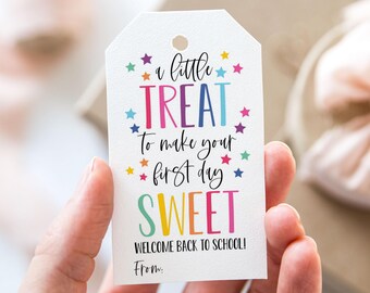 Peut inclure: Une étiquette cadeau blanche avec un motif arc-en-ciel. L'étiquette dit "a little treat to make your first day sweet" et "Welcome back to school!" avec une ligne pour "From:"