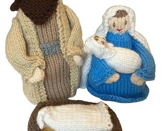 May include: Knitted nativity scene with Joseph, Mary, and baby Jesus in a brown manger. Joseph is wearing a tan robe with a brown beard. Mary is wearing a blue robe and holding the baby. The baby is wrapped in white fabric.