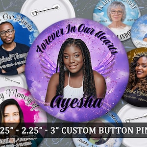 May include: A collection of custom button pins featuring photos of individuals, with text such as "Forever In Our Hearts" and "In Loving Memory." The pins vary in size, with the largest pin featuring a woman named Ayesha. The pins are white with a pin back.