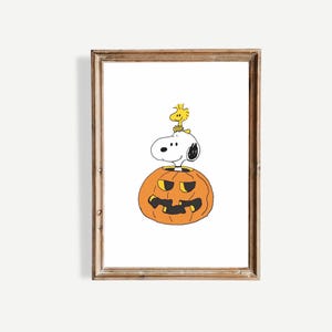 May include: A framed print featuring Snoopy and Woodstock from Peanuts. Snoopy is perched atop a carved orange jack-o'-lantern, with Woodstock sitting on Snoopy's head. The artwork has a white background and a brown wooden frame.