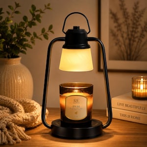 May include: A black metal candle warmer lamp with a handle and a frosted glass shade. The lamp illuminates a dark glass candle jar with a label reading RE CLASSIFIED HEBE the goddess of youth 200g. The lamp base is circular and black.
