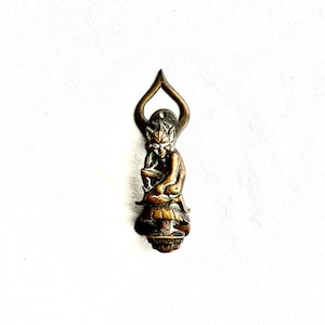 May include: A small, bronze-coloured figurine of a seated figure with a crown and a beard. The figure is holding something in its hands and has a halo-like shape above its head. The figurine is likely a religious or decorative item.