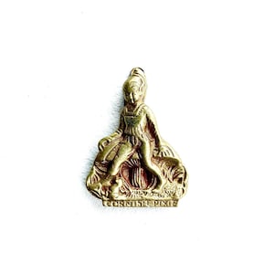 May include: A small, gold-coloured metal figurine of a seated pixie. The pixie is wearing a dress and has a detailed hairstyle. The base of the figurine has the words "CORNISH PIXIE" engraved on it. The figurine is on a white background.