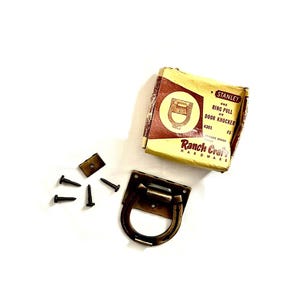 May include: Vintage Stanley ring pull door knocker hardware set. The set includes a brass-toned ring pull, mounting plate, screws, and the original box. The box is tan and maroon with the text "Ranch Craft Hardware".