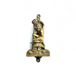 May include: A vintage brass Jack O' Lantern pendant. The pendant features a seated imp figure holding a basket, atop a mushroom-shaped base with the words "Jack O' Lantern". The pendant has a loop at the top for hanging.