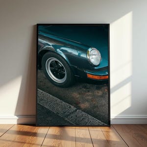 May include: A close-up of a dark teal classic car with a chrome headlight. The car is parked on a street with a kerb and pavement.