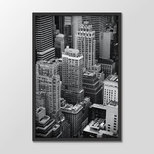 May include: Monochrome framed print depicting a cityscape with many skyscrapers. The buildings are of varying heights and designs, forming a dense urban landscape. The image is taken from a high angle, offering a comprehensive view of the city.