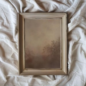 May include: A framed painting of a foggy landscape with trees in the background. The painting is in a light brown frame with a white mat.