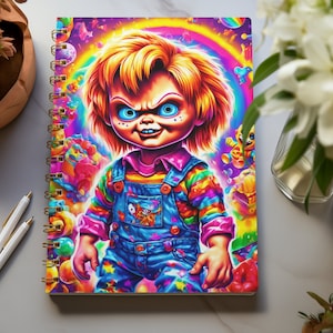 May include: A spiral bound notebook with a colorful illustration of a doll with a menacing expression. The doll is wearing a rainbow striped shirt and blue overalls. The background is a psychedelic rainbow with candy and other colorful objects.