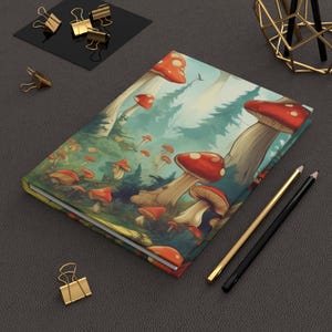 May include: A closed notebook with a colorful illustration of red and white mushrooms in a forest setting. The cover features a whimsical design with green foliage and a blue sky.