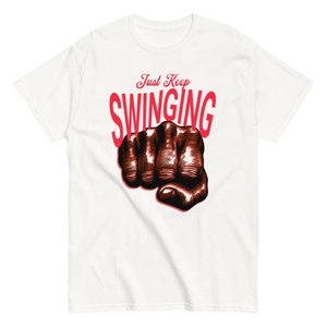 May include: White t-shirt with a red graphic of a fist and the text "Just Keep Swinging".