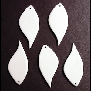 May include: Five white, teardrop-shaped ceramic pendants with a matte finish. Each pendant has a small hole at the top for stringing and a smooth, curved design. The pendants are arranged on a dark brown surface.